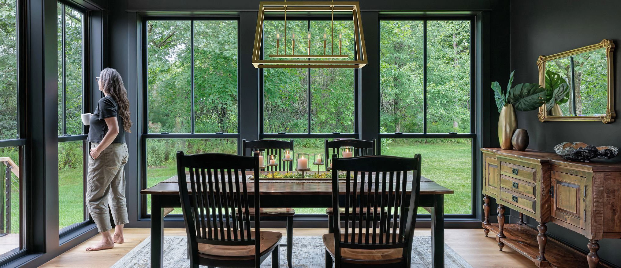Sunlit dining room with floor-to-ceiling Renewal by Andersen windows overlooking the woods